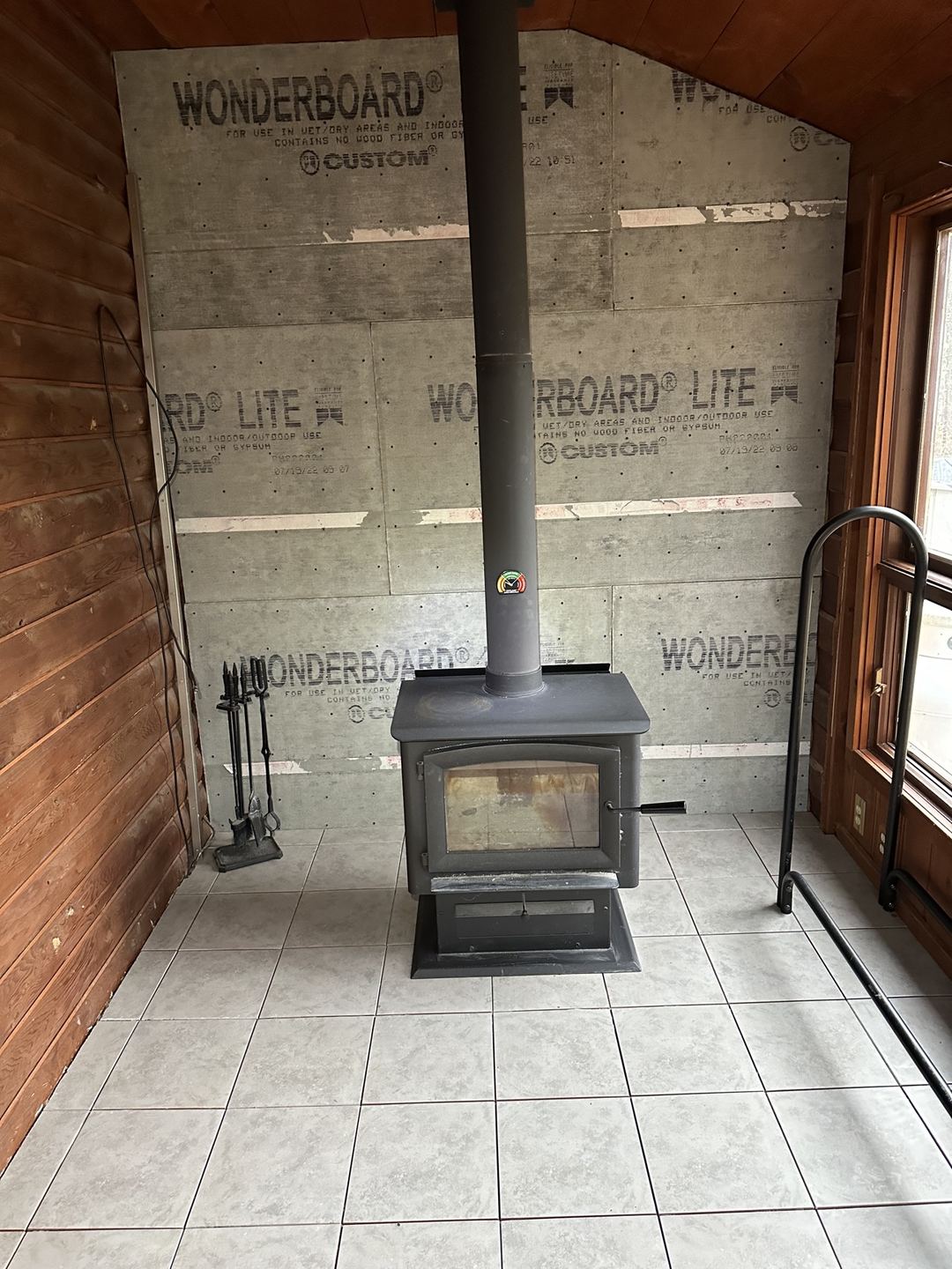 Before: bare cement board wall behind a wood stove, before stone installation